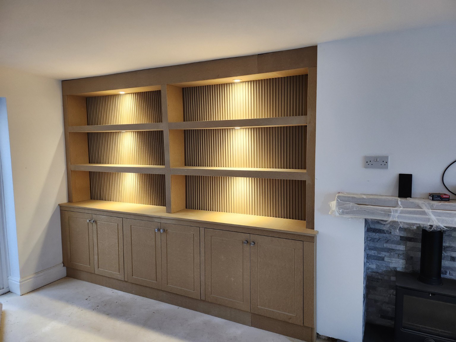 Fitted unpainted alcove cabinets with panelled doors, fluted shelf backs and warm lighting