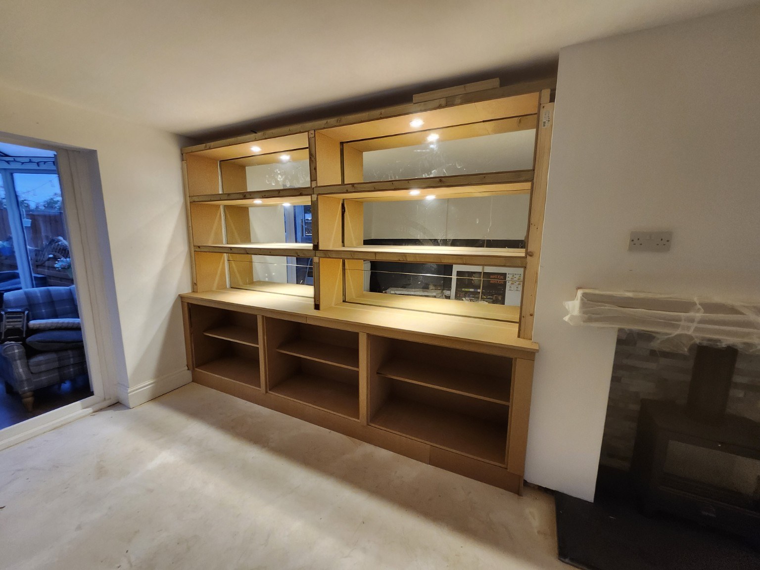 Unpainted alcove shelving with warm spotlights and mirrored backs during construction