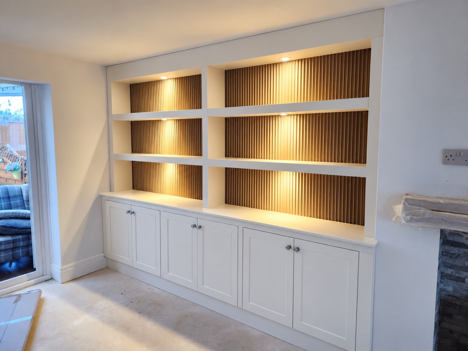 Alcove storage in a white finish with six cupboard doors, fluted shelf backs and warm shelf lighting