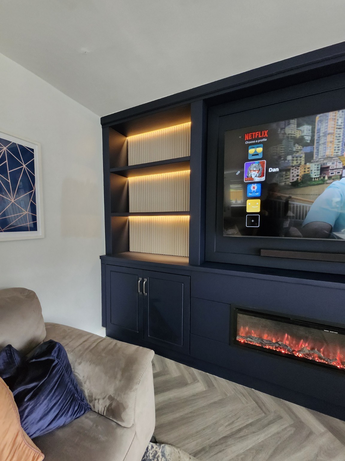 Side view of a navy media wall showing warm LED shelf lighting and cream fluted backs