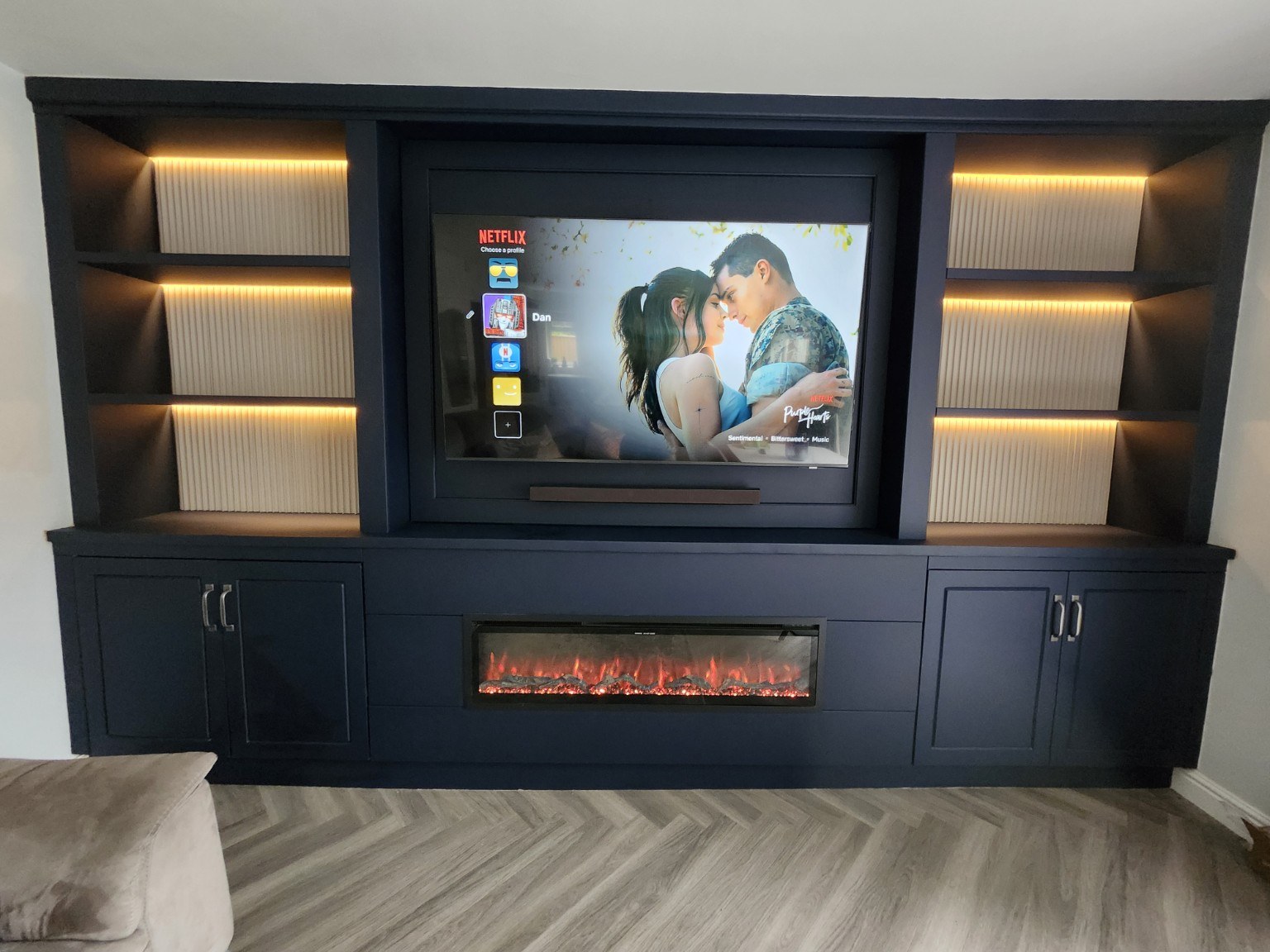 Navy media wall with cream fluted shelf backs, recessed TV, electric fire and fitted storage cupboards