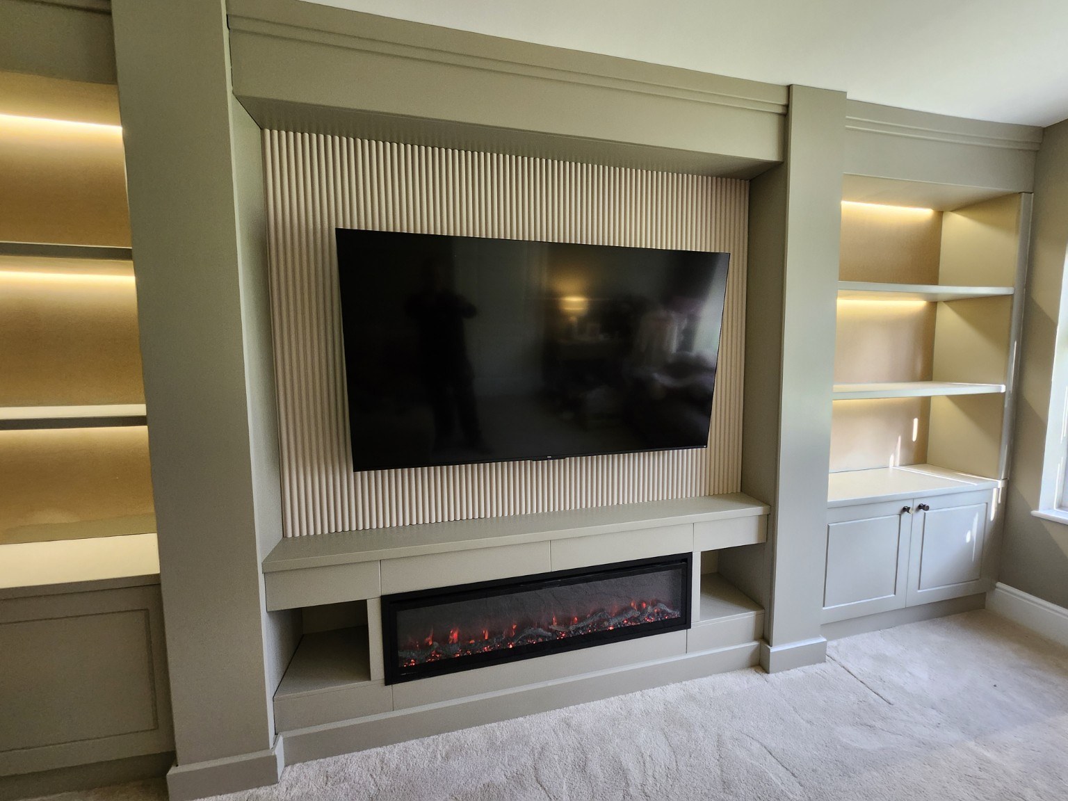 Neutral painted media wall with fluted TV backing, illuminated shelves, electric fire and fitted storage