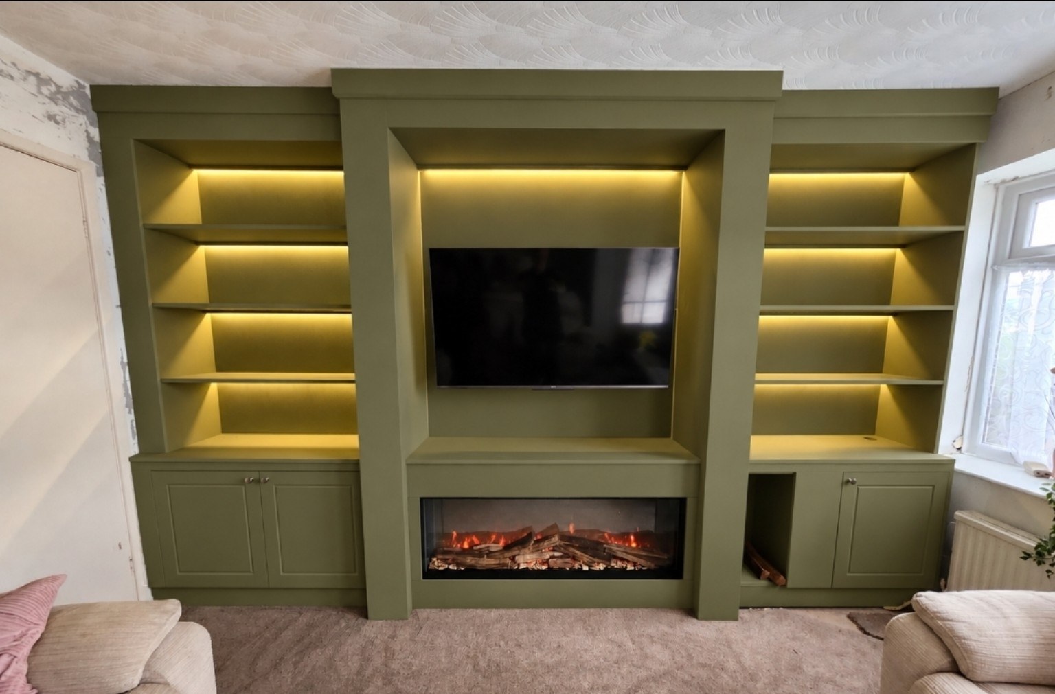 Olive green media wall with recessed TV, electric fire, illuminated shelves and fitted cupboards